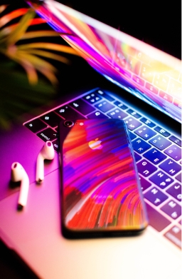 A colourful photo of an iPhone, a couple of AirPods and a Macbook.